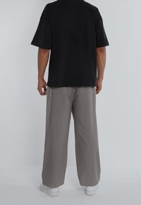 Black oversized t-shirt with short sleeves, paired with light gray wide-leg pants and white sneakers. Simple, casual design.