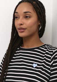 Black and white striped t-shirt featuring a light blue heart patch on the left side. Smooth fabric with a classic crew neckline.