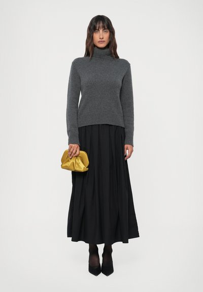 Grå turtleneck genser laget av strikket stoff, kombinert med et svart langt skjørt og holder en sennepsgul clutchveske. Svarte høye hæler.