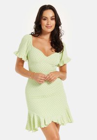 Green polka dot dress made of lightweight fabric, featuring a fitted bodice, short ruffled sleeves, and a flared hem with ruffle accents.