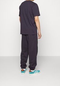 Camiseta de algodón gris oscuro y pantalones jogger a juego, con puños elásticos. Zapatillas en azul petróleo con suela blanca y detalles en burdeos. Diseño sencillo.