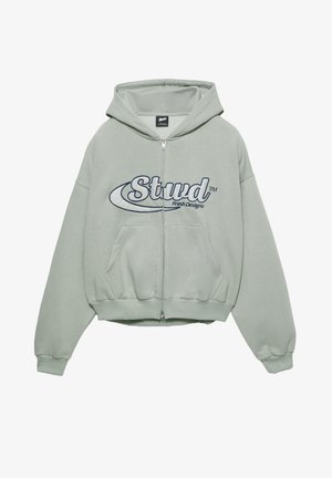 Hanorac cu fermoar verde deschis, cu buzunar frontal. Prezintă logo-ul "Stud" în albastru închis, mâneci și tiv cu margini striate. Material moale, texturat.