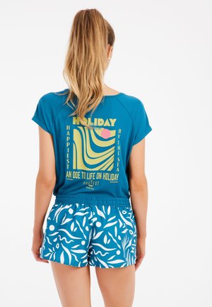 Camisa azul de manga corta con texto colorido y diseño gráfico en la parte posterior, combinada con pantalones cortos de rayas azules y blancas.