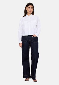 White cropped button-up shirt with two chest pockets; paired with dark blue wide-leg denim jeans featuring contrast stitching and back pockets.