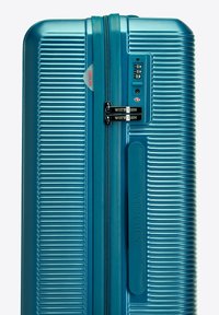 Tyrkysový tvrdý kufr s rýhovaným designem, dvojitými zipy a integrovaným kombinačním zámkem. Obsahuje branding na táhle zipu.