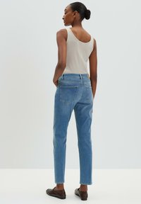Débardeur gris clair associé à un jean en denim bleu taille haute. Les jeans présentent une coupe classique et deux poches plaquées au dos. Texture de tissu lisse.