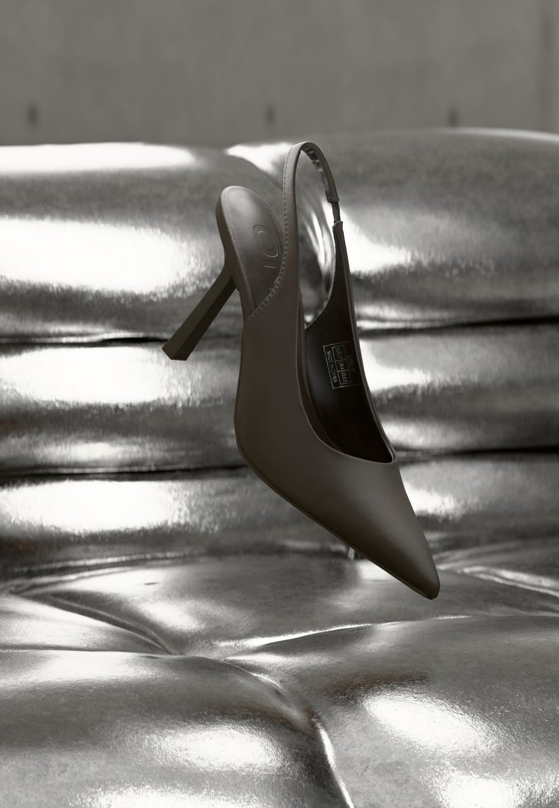 Μαύρο μυτερό γόβα με τακούνι και λουράκι στην πλάτη, ακουμπισμένο σε μια λαμπερή, μεταλλική ασημένια επιφάνεια με κουμπιά.