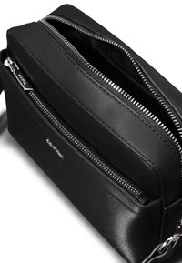Sort lædertaske med to lynlåslommer, glat tekstur og sølvfarvede metaldele. Kompakt, rektangulært design med minimalistisk udseende.