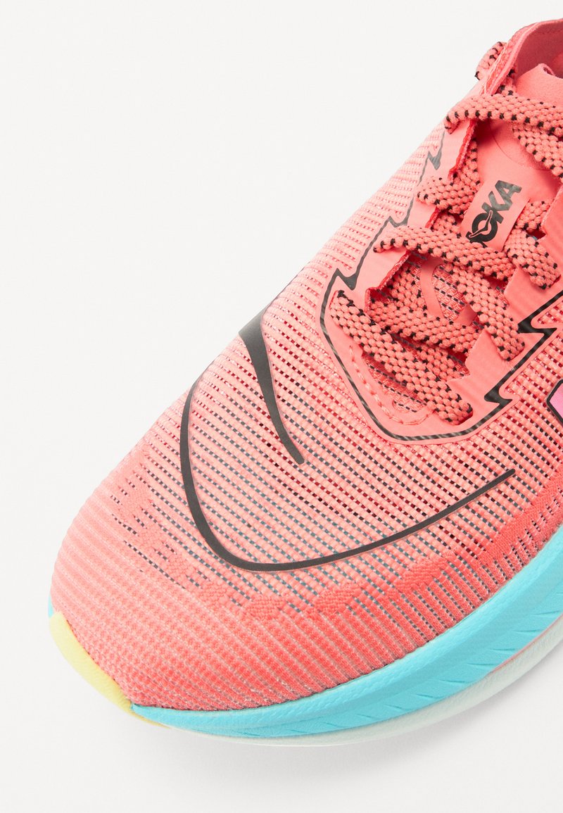 Chaussure de course légère en corail vif avec tige en maille, accents noirs et semelle turquoise. Présente une surface texturée et un design à lacets.