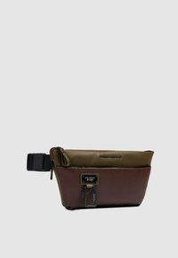 Bolso bandolera de cuero marrón y verde con cierre de cremallera, correa ajustable y un detalle metálico con una etiqueta de logotipo en el frente.