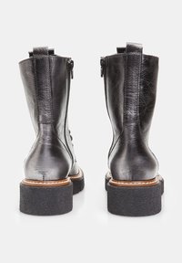 Bottines en cuir noir avec une finition texturée, fermeture éclair à l'arrière et une semelle en caoutchouc noir épaisse. Présente un bord cousu marron le long de la semelle.