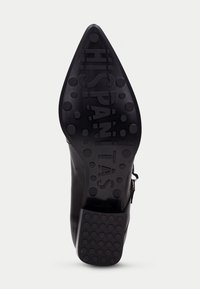 Suela de zapato de cuero negro con punta afilada, que presenta una superficie texturizada y patrones de agarre circulares. "HISPANITAS" está grabado en la suela.