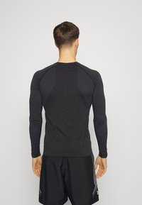 Langärmliges Sportshirt, dunkelgrau mit strukturierten schwarzen Streifen an den Schultern und Seiten, gefertigt aus leichtem, feuchtigkeitsableitendem Material.