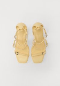 Yellow heeled sandals with a smooth finish, square toe, and ankle straps. Features silver buckles and a low block heel for support.