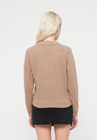 Pull marron texturé avec un col et des manches longues, cintré à la taille, porté avec une mini-jupe noire, vu de dos.