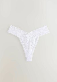 Perizoma bianco in pizzo con motivi floreali, bordi scallop e una texture semitrasparente. Progettato per posizionarsi basso sui fianchi.