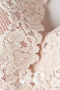 Krajková látka v jemně béžové barvě s květinovými vzory, zdobená vroubkovanými okraji a kombinací hustě tkaných a otevřených pletenin, které přidávají texturu.