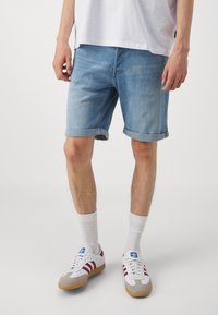 Svetle modré riflové šortky s ohrnutými manžetami a klasickým pětipocket designem, spárované s bílými ponožkami ke kotníkům a teniskami s červenými a šedými akcenty.