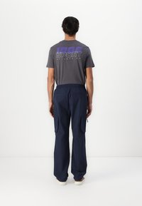 Gray short-sleeve T-shirt with "1665 SPORT ATLANTA US" printed in white and purple, paired with navy cargo pants featuring side pockets.
