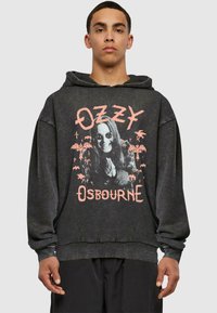 Sort hoodie med et grafisk print af en mand i solbriller, omgivet af palmetræer og flagermus, fremhævet af lyserøde bogstaver med teksten "Ozzy Osbourne."
