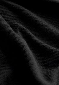 Tessuto a maglia nero con una superficie morbida e texturizzata, che mostra pieghe e increspature delicate, enfatizzando profondità e dimensionalità.