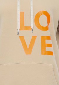 Hoodie beige avec un grand imprimé orange "LOVE", des cordons avec un texte répétitif et une poche frontale. Texture lisse.