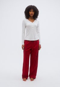 Haut henley blanc à manches longues avec trois boutons ; pantalon de pyjama rouge présentant des motifs floraux noirs et une coupe décontractée.