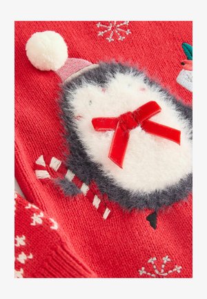 Piros kötött ruhadarab, amelyen pingvin motívum látható fehér bolyhos részletekkel, rózsaszín sapkával, piros masnival és cukormentás mintával. Lágy textúra látható.