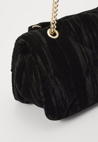 Borsa a tracolla in velluto trapuntato nero con manico a catena dorata, caratterizzata da una texture morbida e una forma arrotondata, che mette in risalto dettagli di cucitura eleganti.