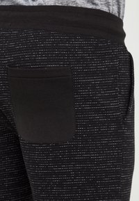 Mustad dressipüksid taktilise horisontaalse triibumustriga. Varustatud tagatasku ja elastse vöökohaga. Valmistatud pehmest, venivast materjalist.