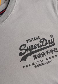 Grijs katoenen t-shirt met een ronde hals en een zwarte grafische print met de tekst "SuperDry" en Japanse tekens.