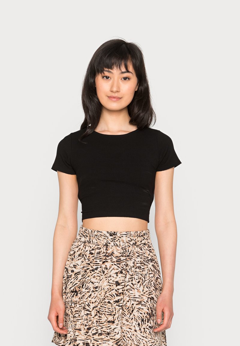 Top curto preto com textura canelada e mangas curtas, combinado com uma saia estampada em tons de laranja, preto e creme, contra um fundo neutro.