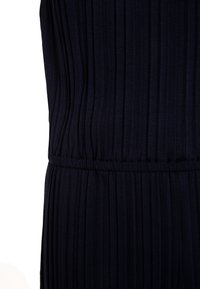 Tmavě námořnický overal s vertikálními plisemi, s elastickým pasem a hladkou texturou. Tkanina se zdá být lehká a jemně splývavá.