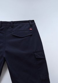 Pantaloni blu marina che mostrano la vita posteriore, tasca con pattina con etichetta della bandiera norvegese, tasca cargo laterale, passanti per cintura, su uno sfondo grigio chiaro.