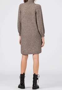Brun stickad klänning med hög halsringning, långa ärmar och avslappnad passform, i kombination med svarta snörda ankelskor.