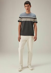 Kortærmet t-shirt med blå, grå og hvide vandrette striber; sat sammen med hvide bukser og hvide sneakers. Glat tekstur.