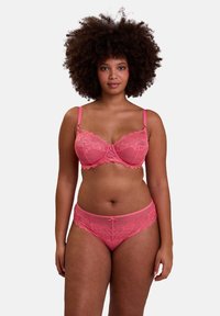 Ensemble de lingerie en dentelle rose comprenant un bralette avec des bords en feston et des bretelles ajustables, associé à un slip assorti avec des bordures en dentelle.
