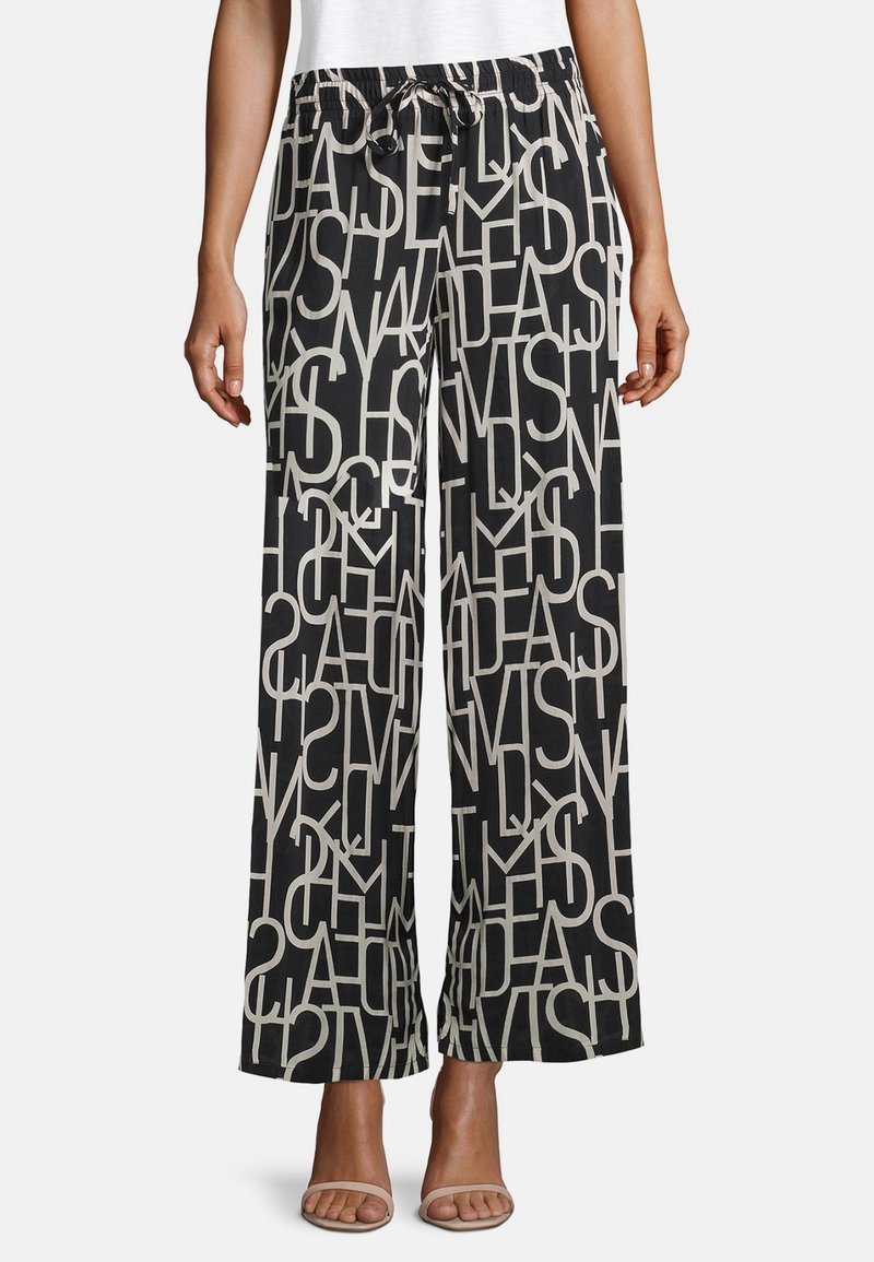 Černé kalhoty s širokými nohavicemi a bílými překrývajícími se velkými písmeny, elastický pas se šňůrkou, nošeno s bílými sandály a bílým topem.