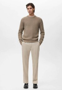 Suéter de punto acanalado beige con cuello redondo, combinado con pantalones beige claros de corte ajustado y zapatos negros, con piernas rectas y una textura suave.