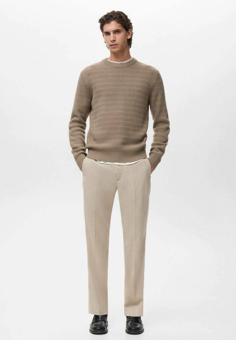 Maglione a coste beige con scollatura rotonda, abbinato a pantaloni beige chiaro su misura e scarpe nere, caratterizzati da gambe dritti e una texture morbida.