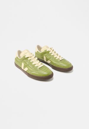 Paar grüne Sneaker mit niedrigem Schaft, cremefarbenen Schnürsenkeln, beigen Fersenschlaufen und dunkelbraunen Gummisohlen auf weißem Hintergrund.