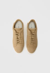 Τα καφέ σουέτ αθλητικά παπούτσια με λευκές λαστιχένιες σόλες, στρογγυλή μύτη και κλασικό σχέδιο με κορδόνια. Το εσωτερικό διαθέτει το λογότυπο της μάρκας και μαλακή επένδυση.