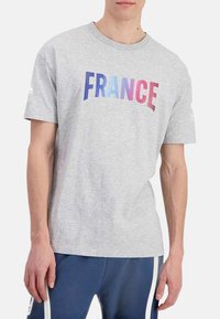 T-shirt en coton gris avec le mot "FRANCE" en lettres dégradées bleu et rose sur la poitrine, manches courtes et col rond.
