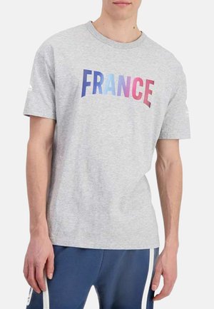 T-shirt en coton gris avec le mot "FRANCE" en lettres dégradées bleu et rose sur la poitrine, manches courtes et col rond.