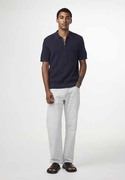 Laivastonsininen lyhythihainen polo, jossa on vetoketju, ribbiteksturilla. Yhdistetty vaaleanharmaisiin suoralahkeisiin farkkuihin ja mustiin liukusandaaleihin.