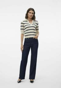 Gestreepte gebreide trui in crème en marineblauw, V-hals, korte mouwen, gecombineerd met donkerblauwe wijde jeans en zwarte puntige hakken.