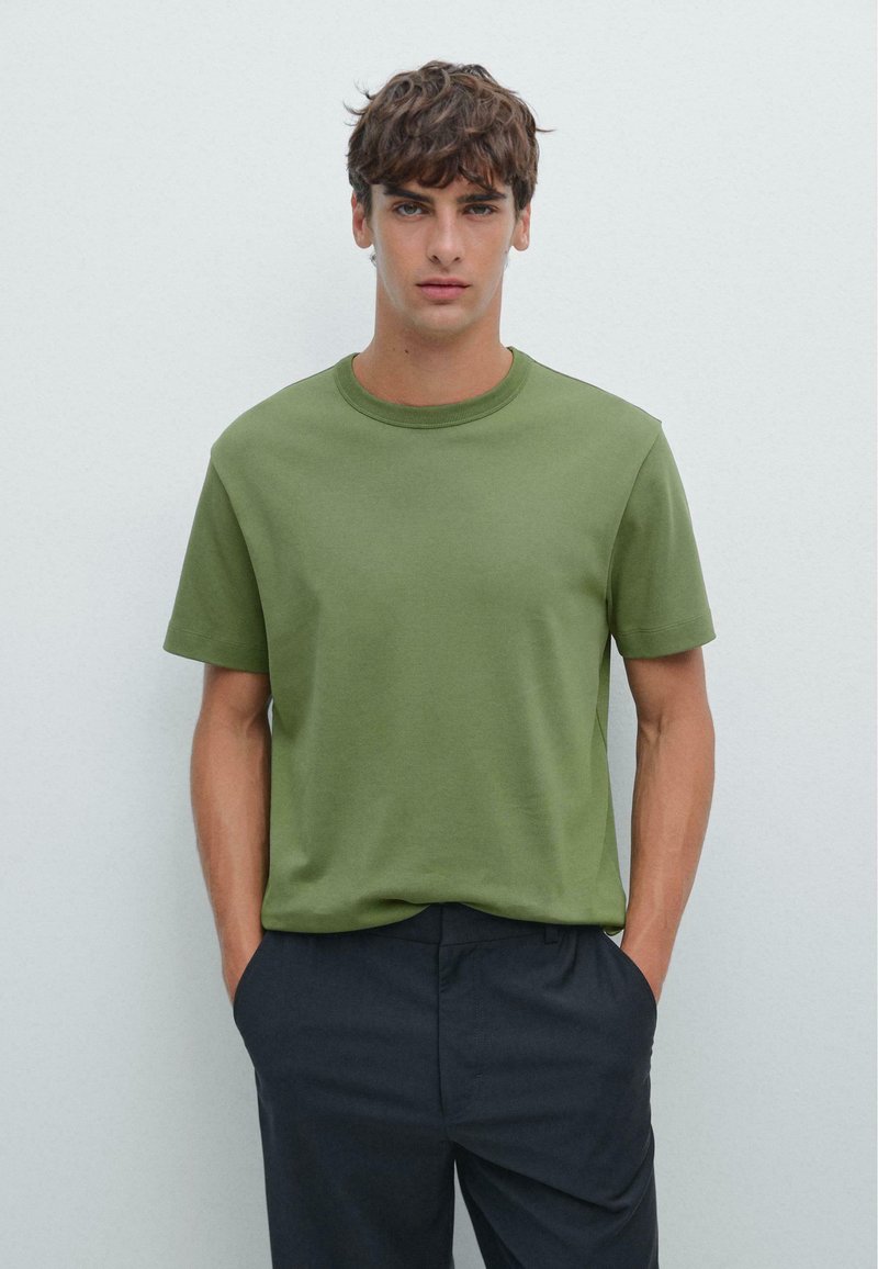 Groen katoenen T-shirt met korte mouwen en een ronde hals, gecombineerd met een donkere broek. Eenvoudig ontwerp en gladde textuur.