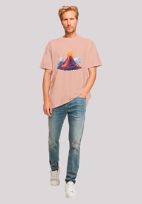 Pink short-sleeve t-shirt featuring a colorful volcano graphic; paired with light blue distressed jeans and white sneakers.
