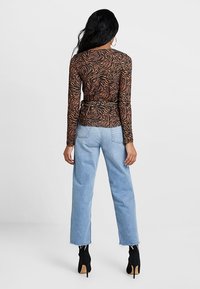 Langärmliges braunes Oberteil mit einem schwarz-orangen Wellenmuster, kombiniert mit hellblauen hochtaillierten Jeans und schwarzen Stiefeletten mit Absatz.