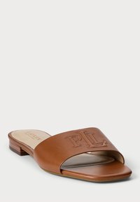 Σαγιονάρες από καφέ δέρμα με φαρδιά λωρίδα που φέρει ανάγλυφα αρχικά. Χαμηλή ξύλινη φτέρνα και λεία σόλα. Ανοιχτό μπροστινό σχέδιο.